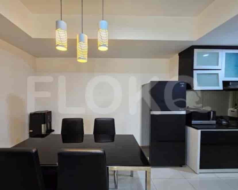 A dining area with a black table and chairs, and a kitchen with a refrigerator and cabinets.