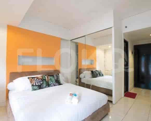 A well-lit bedroom featuring a bed, a large mirror, and a hint of a kitchenette.