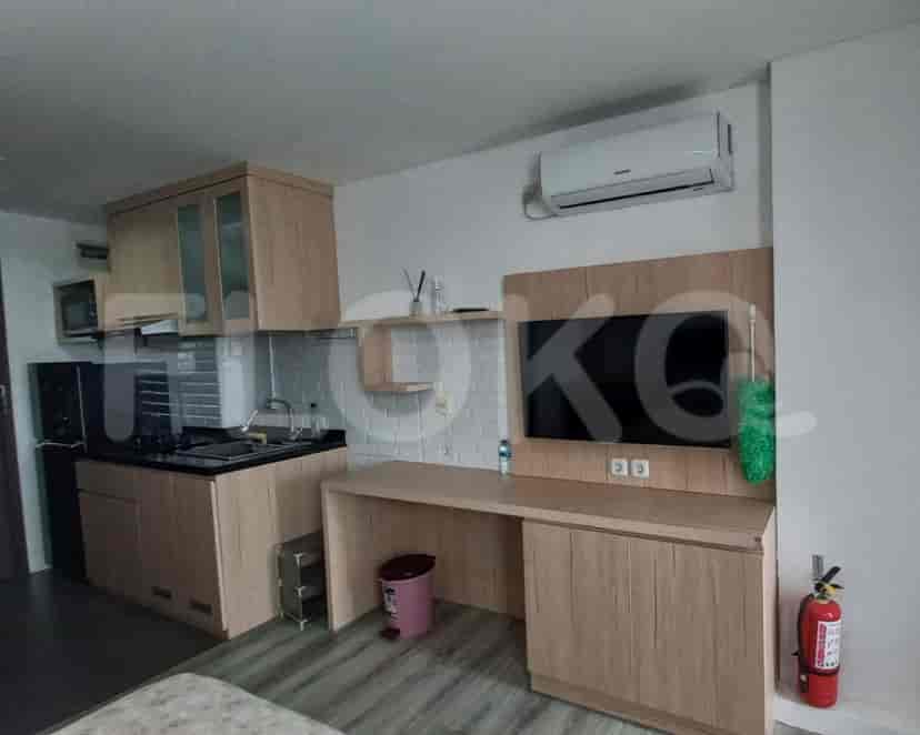 A compact kitchenette with a wooden cabinet, a flat-screen TV, and appliances.