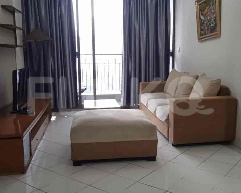 A living room with a brown sofa, ottoman, TV stand, and a large window.
