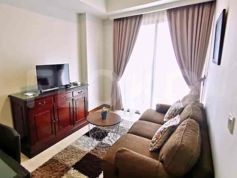 Ruang tamu dengan sofa coklat, lemari kayu, dan jendela besar dengan gorden tipis.