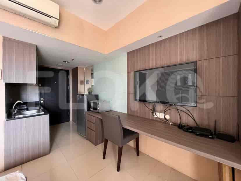 A small studio apartment featuring a kitchenette area with a desk, TV, microwave, and a dark-colored door.