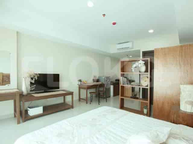 A combined bedroom and living area with a bed, entertainment unit, and a small dining area.