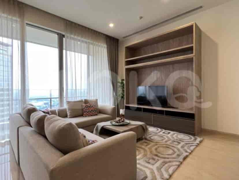 A spacious living room with an L-shaped grey sofa, wall-mounted smart TV, and large window with sheer curtains.