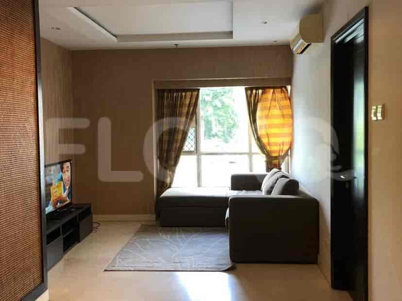A well-lit living room features an L-shaped grey sofa, a TV, and a large window with curtains.