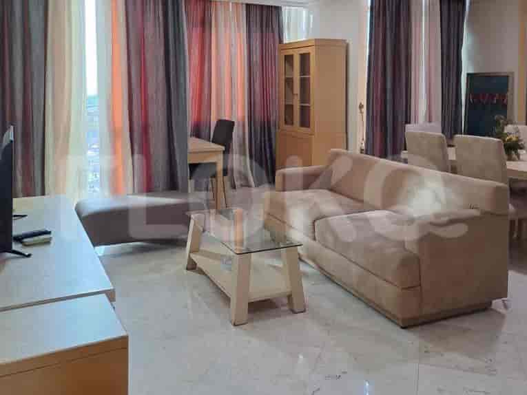 A living room with a beige sofa, glass table, and large windows.