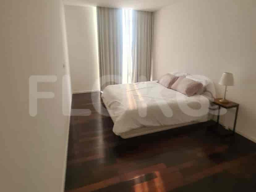 A bedroom with a comfortable bed, neutral-toned decor, and large windows with curtains.