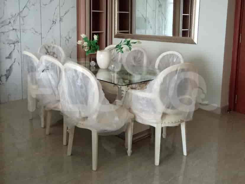 A dining room with a glass-topped table, white chairs covered in protective plastic, and a marble accent wall.