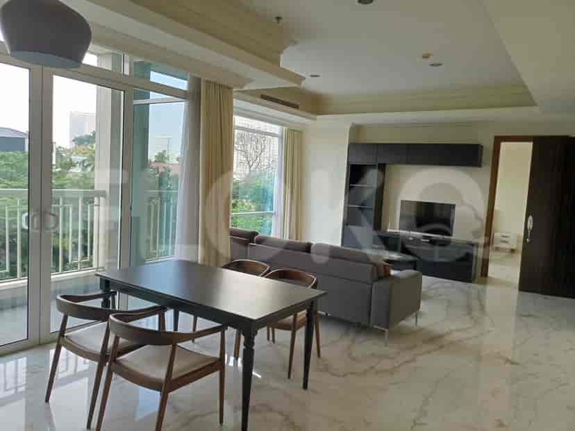 Ruang tamu dan ruang makan yang cerah dengan meja makan dan kursi kayu gelap, jendela besar, dan akses ke balkon.
