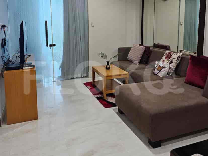 A spacious living room with an L-shaped grey sofa, wall-mounted smart TV, and large window with sheer curtains.