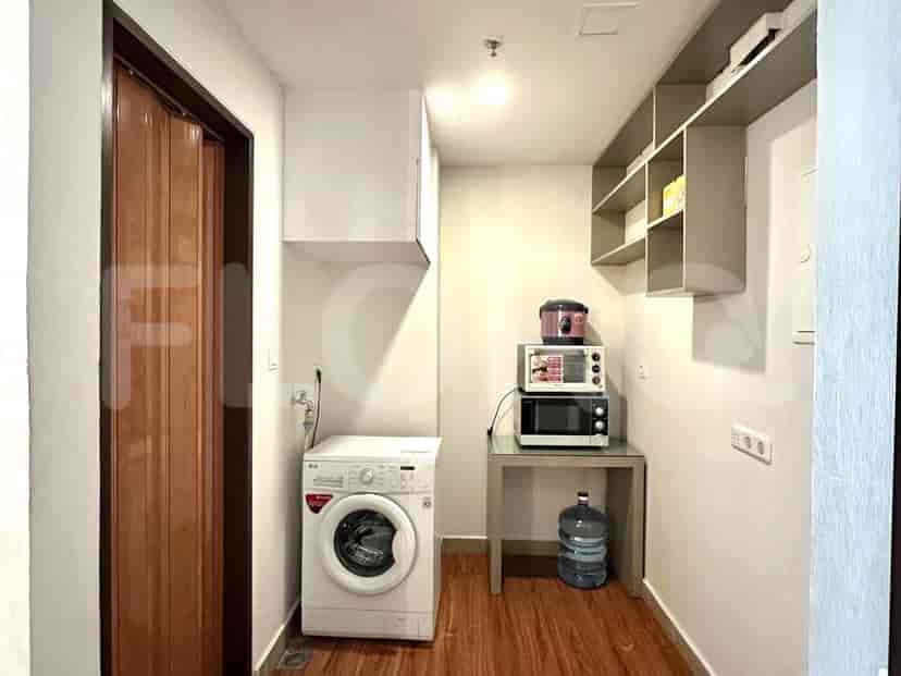 Laundry room with a washing machine, a shelf of stored items, and additional space for storing cleaning supplies.