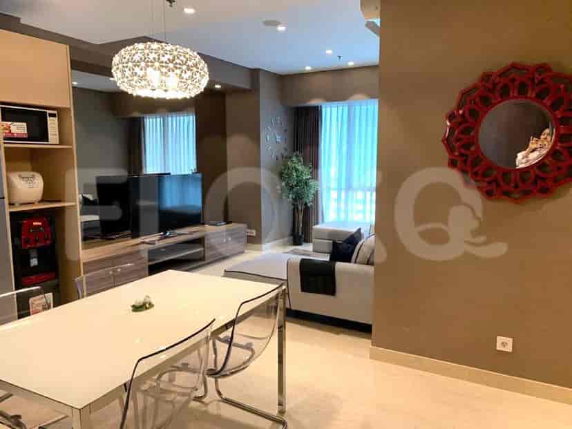 Ruang tamu modern dengan area makan yang menampilkan meja makan dengan kursi bening, sofa, dan unit TV.