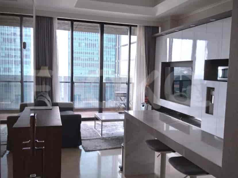 A modern living room with a grey sofa, a wall-mounted TV, and large windows offering a city view.