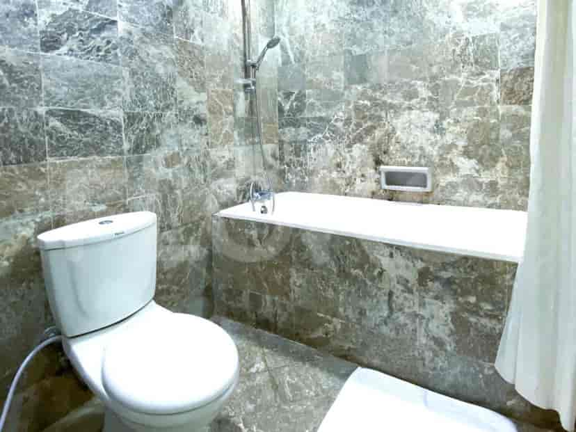 Kamar mandi yang menampilkan bak mandi dan toilet, dengan finishing ubin marmer.