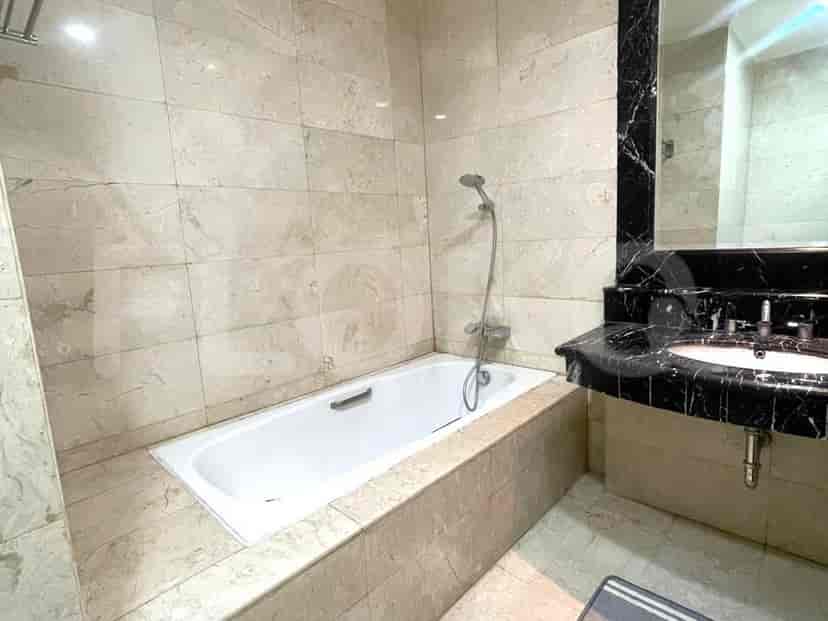 A bathroom with marble tile walls and floor, a white bathtub, a marble vanity with a sink, and a large mirror.