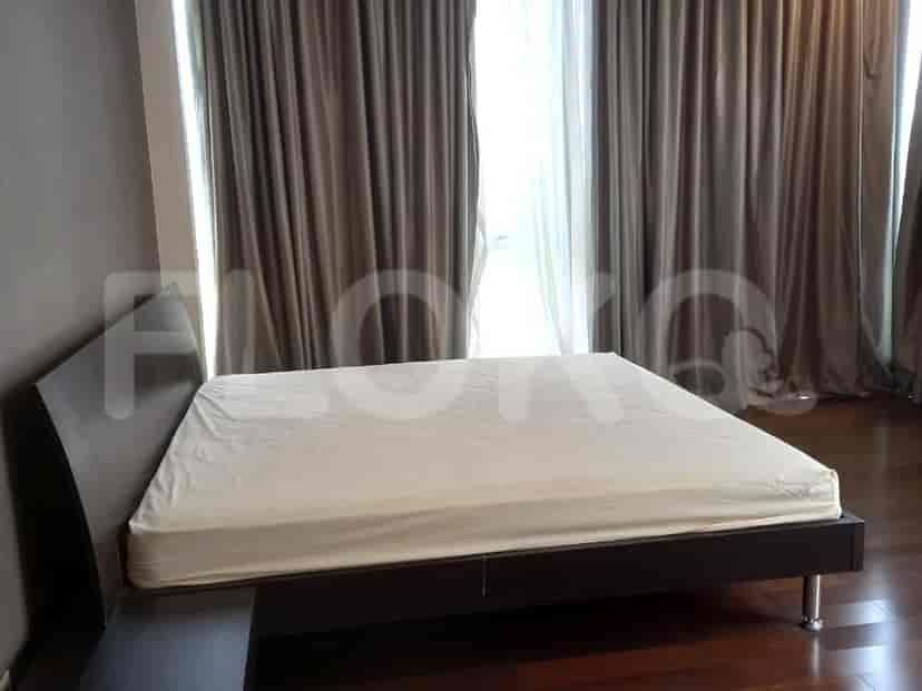 A bedroom with a bed frame and large windows with curtains.