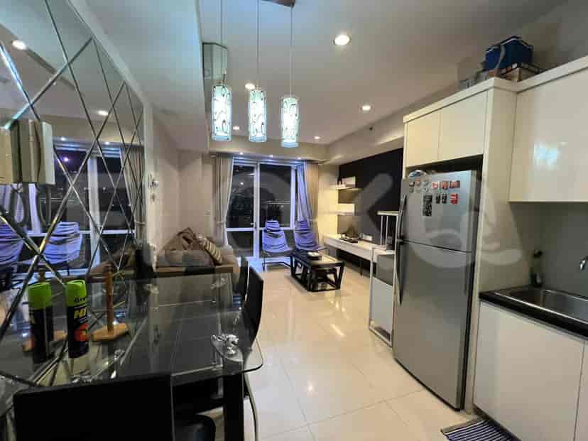 Pemandangan ruang tamu dengan dapur di belakang, menampilkan meja makan, sofa, dan berbagai peralatan.