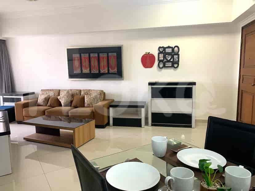 Living area with a brown sofa, artwork, and a dining table in the foreground.