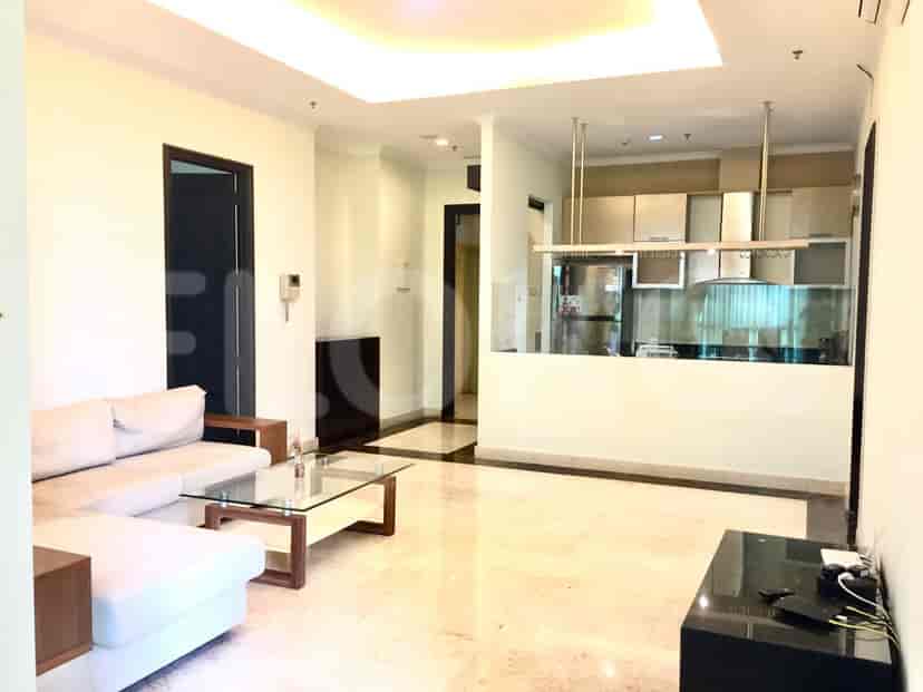 A modern living room with a white sofa, glass coffee table, and open kitchen.