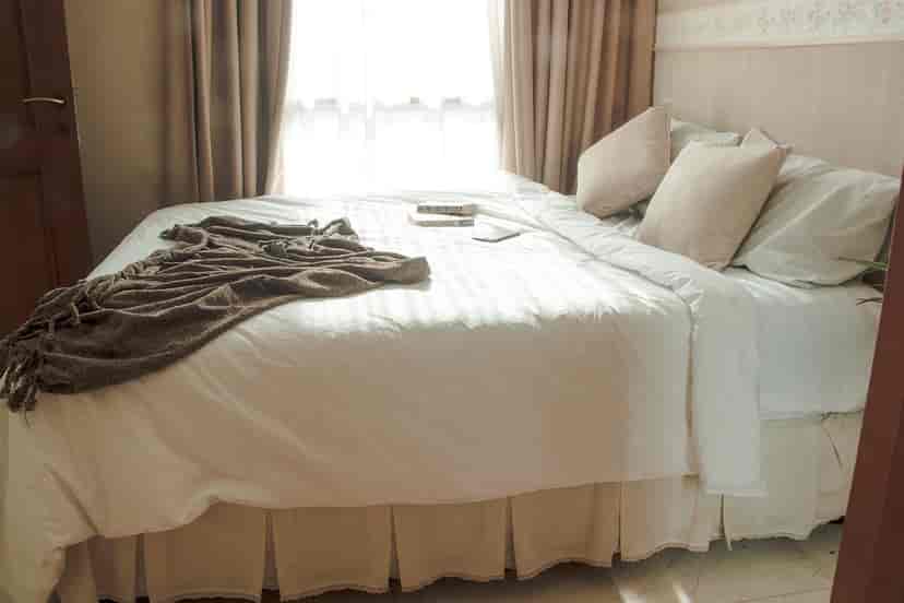 A bright bedroom with a bed, white linens, and a window.