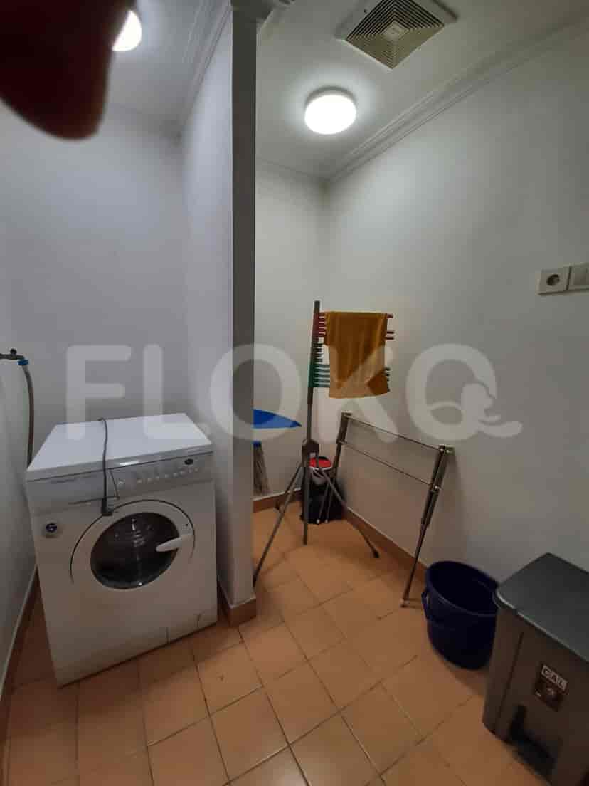 A laundry room with a washing machine, drying rack, and trash bin.