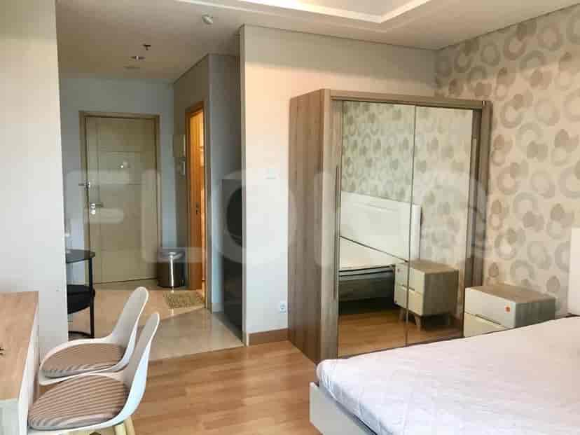 A studio apartment bedroom with wooden flooring, a mirrored wardrobe, and a hallway leading to other rooms.
