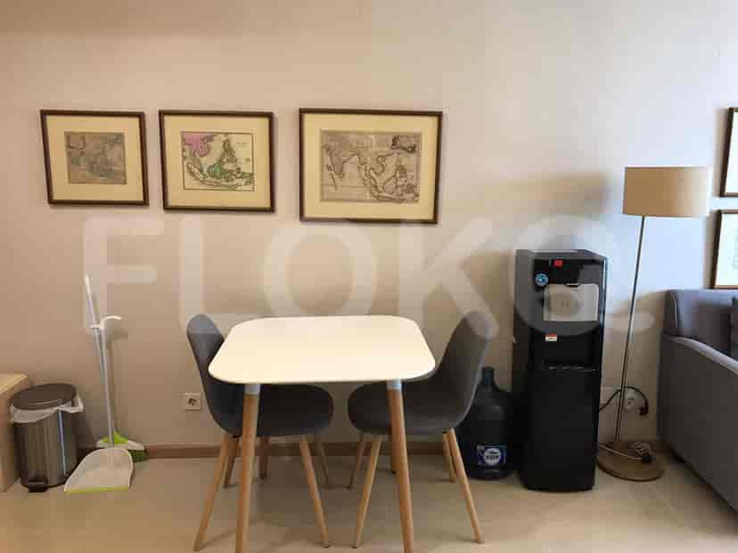 A dining area featuring a white square table with two grey chairs and framed antique maps on the wall.