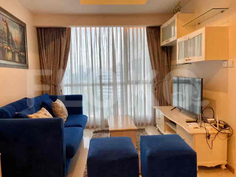 Ruang tamu dengan sofa biru, ottoman, dan TV, di samping jendela besar.