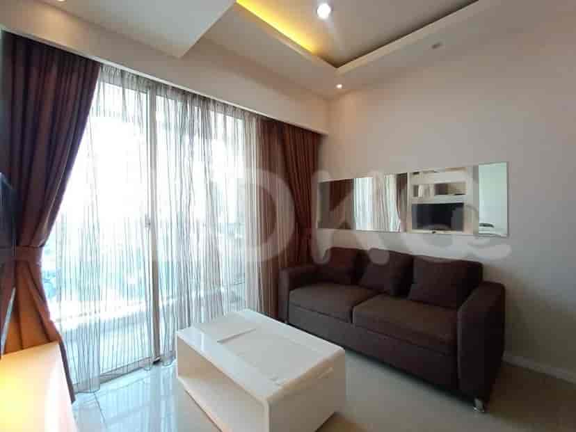 Ruang tamu bergaya dengan sofa abu-abu, TV, dan pemandangan kota melalui gorden tipis.