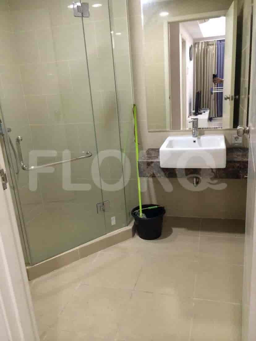 Kamar mandi dengan kandang pancuran kaca, wastafel modern, dan ubin bernada netral.