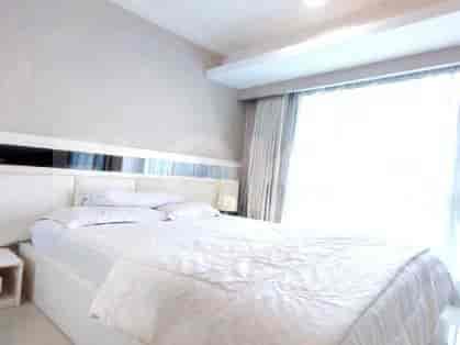 Bedroom with white bed, nightstand and large windows.