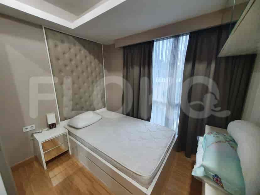Kamar tidur modern yang menampilkan tempat tidur dengan sandaran kepala berumbai, meja samping tempat tidur, dan jendela besar.