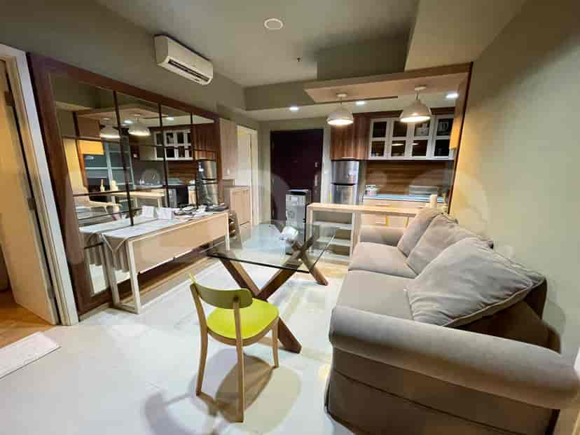 A combined living room and kitchen space with a sofa, glass table and kitchen area.
