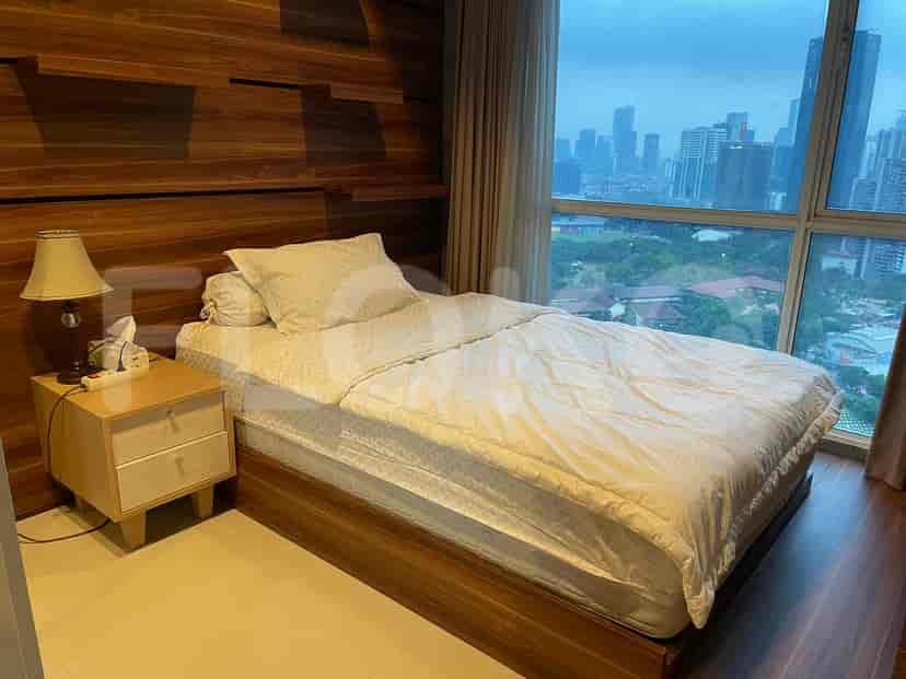 A bedroom with a bed, a nightstand, and large windows.