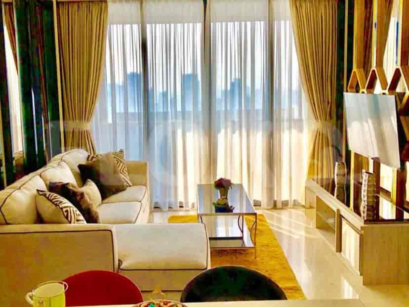 A spacious living room with an L-shaped beige sofa, a smart TV, and large windows with sheer and blackout curtains.