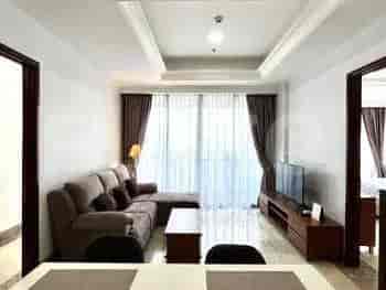 A spacious living room with an L-shaped grey sofa, wall-mounted smart TV, and large window with sheer curtains.