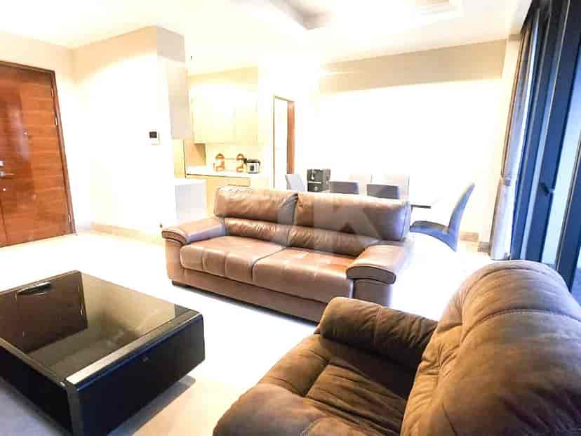 Another view of the living room showcasing a sofa, armchair, and dining table, with access to the kitchen.