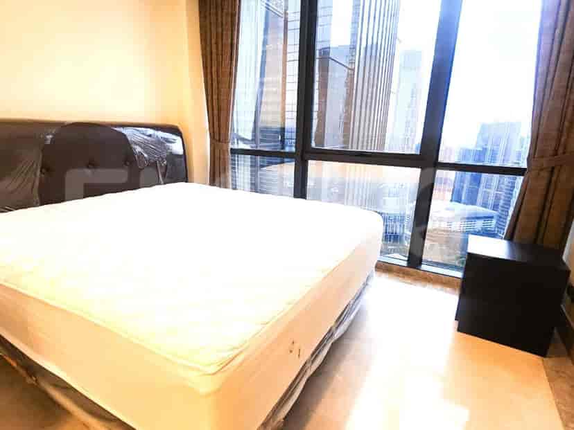 A bedroom with a bed, large windows offering a city view, and a nightstand.