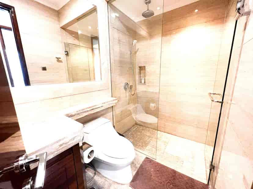 A modern bathroom with a glass shower, large mirror, and marble finishes.