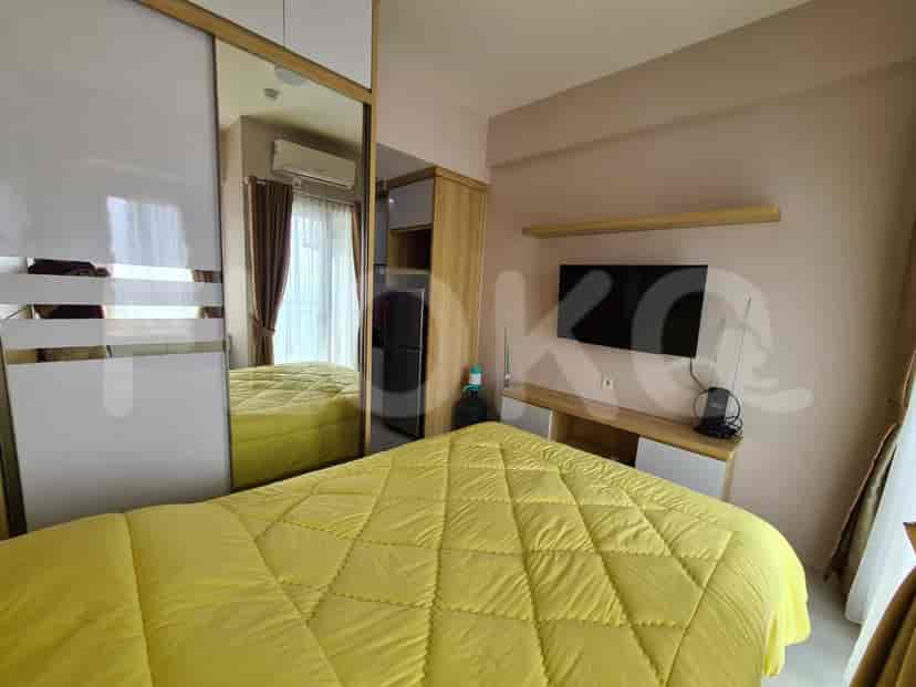 A bedroom with a yellow quilt, a large TV, and a window overlooking the city.