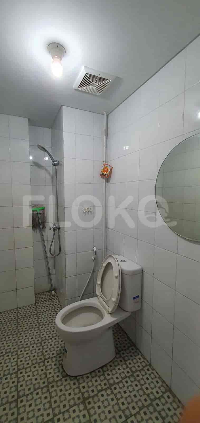 A clean, white-tiled bathroom with a toilet, shower, and mirror.