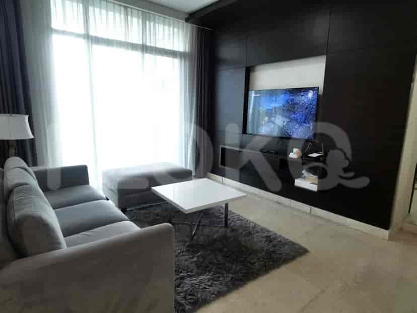 A modern living room with a grey sofa, a wall-mounted TV, and a large window.