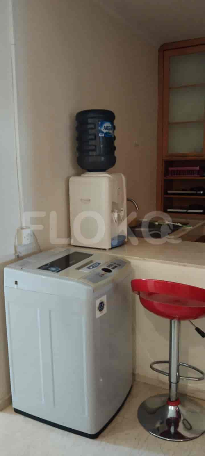 A modern kitchen with a washing machine, water dispenser, and red bar stool.