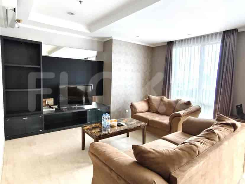 Ruang tamu modern dengan sofa cokelat, TV besar, dan pemandangan melalui gorden tipis.