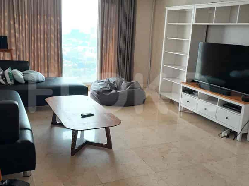 Ruang tamu modern dengan sofa abu-abu, rak buku putih, dan TV besar.
