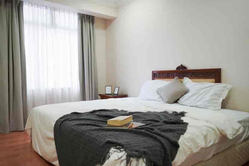 Kamar tidur dengan tempat tidur, meja samping tempat tidur, dan jendela dengan gorden.