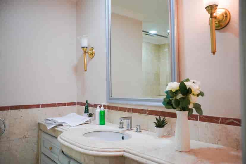 Kamar mandi dengan wastafel, cermin, dan rangkaian bunga.
