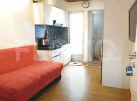Apartemen studio kecil dengan sofa merah, dapur terbuka, dan pintu menuju ke luar.