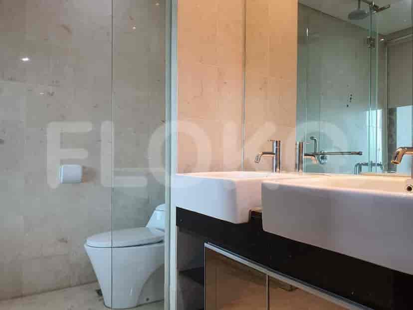 A modern bathroom with a double sink vanity, and a view of a toilet behind a glass partition.