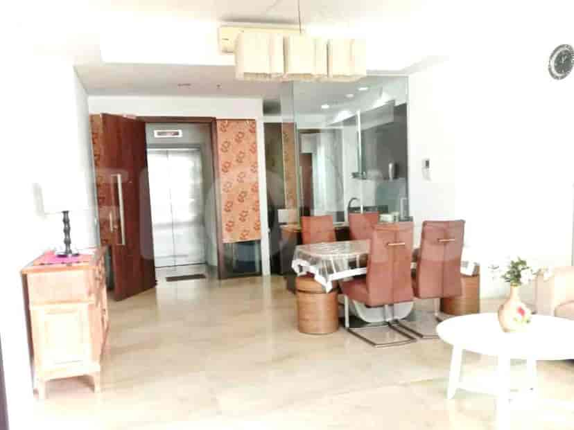 A dining room with a glass table, brown chairs, and a view into a kitchen.